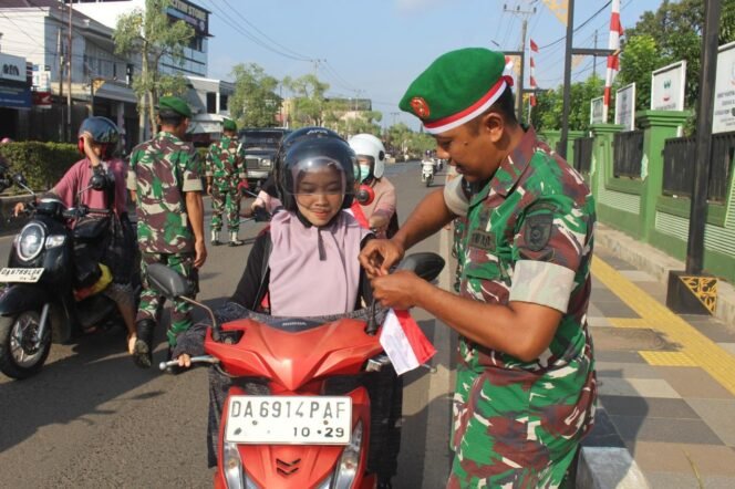 
					Personel Kodim 1009 Tanah Laut membagikan bendera merah putih kepada pengguna jalan yang melintas depan Makodim, Selasa (5/8/2025).